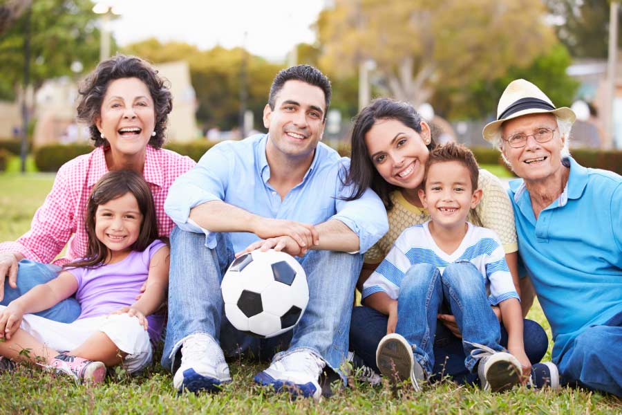 Smiling multigenerational Hispanic family sitting on the grass with a soccer ball