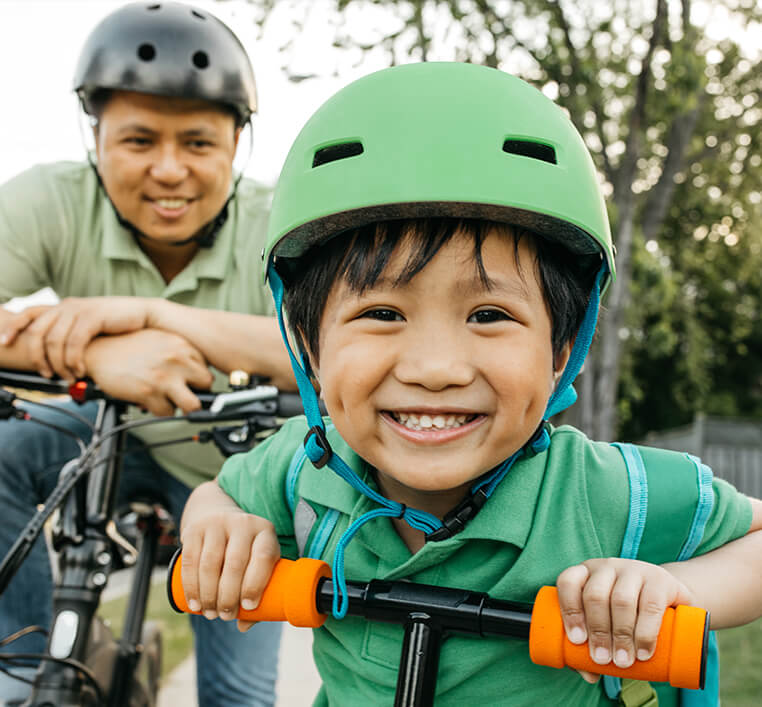 young boy on bike with his dad behind him