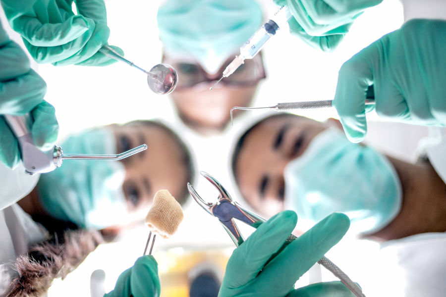 Masked dental professionals looking down on patient as they prepare for oral surgery.