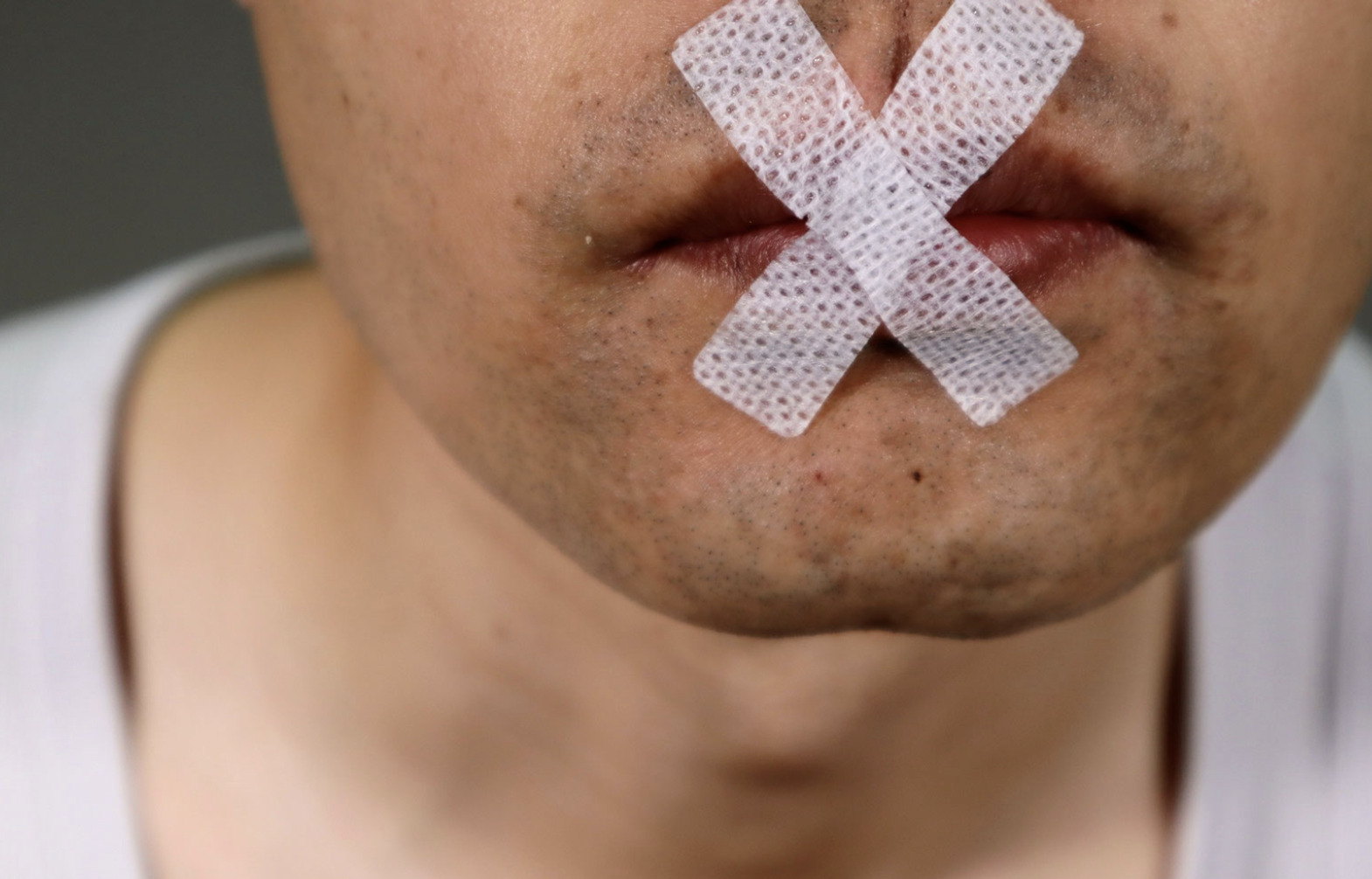 man with X shape medical tape covering his mouth