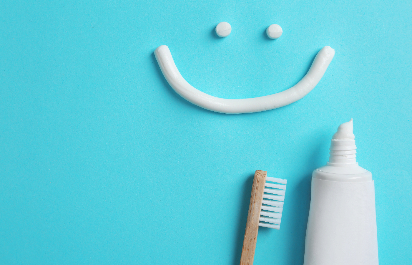 blue background with bamboo toothbrush and toothpaste with a smiley face made of toothpaste..