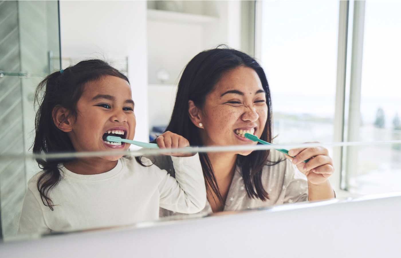 View of mom and daughter brushing their teeth in the mirror