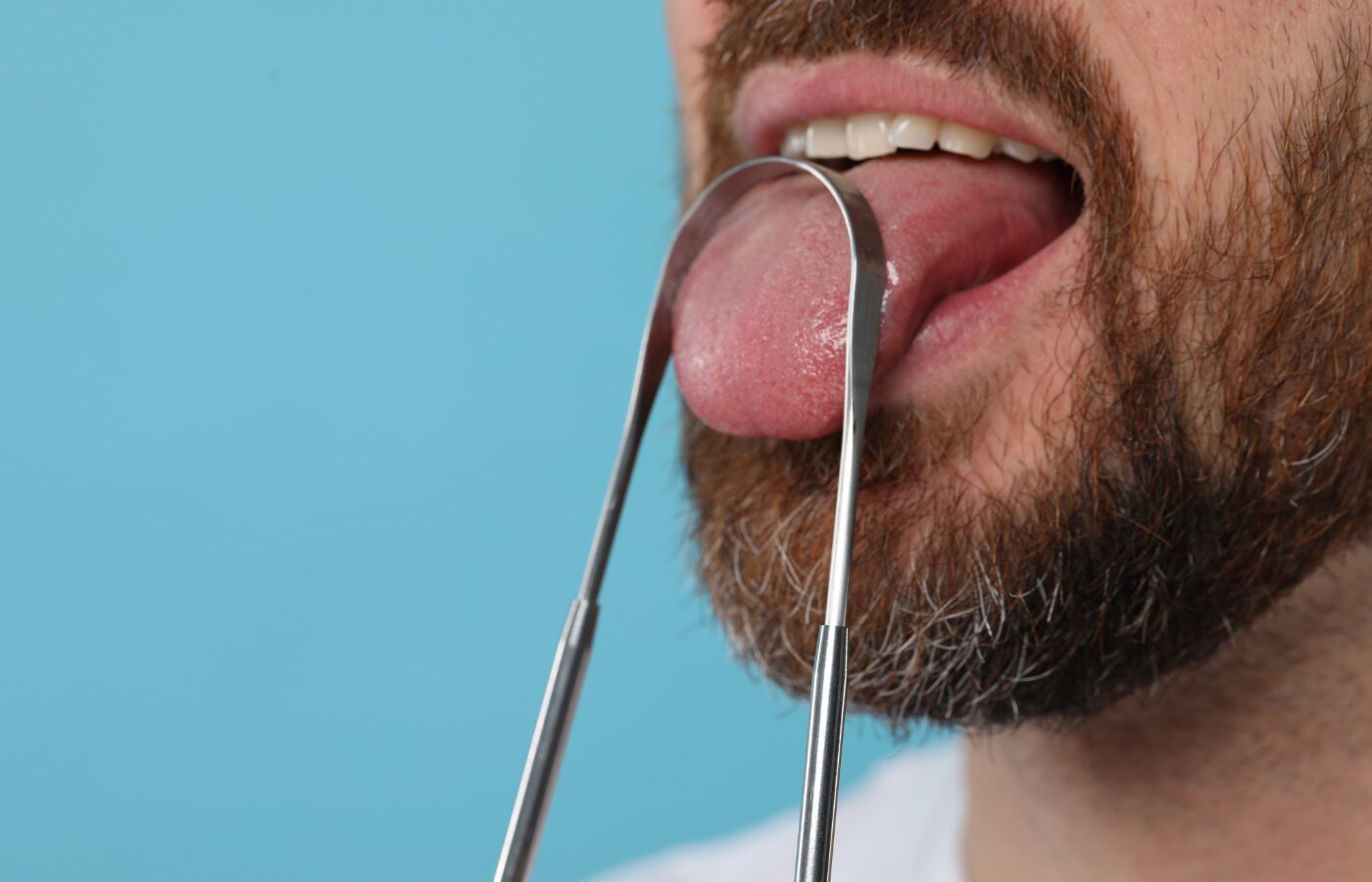 Blue background with man using a metal tongue scaper on his tongue