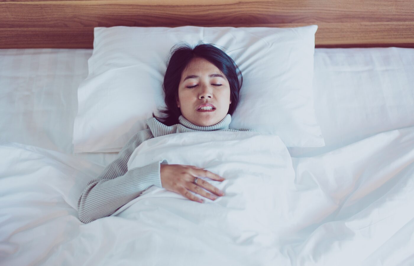 Woman in a bed with white sheets and eyes closed. Grinding her teeth.