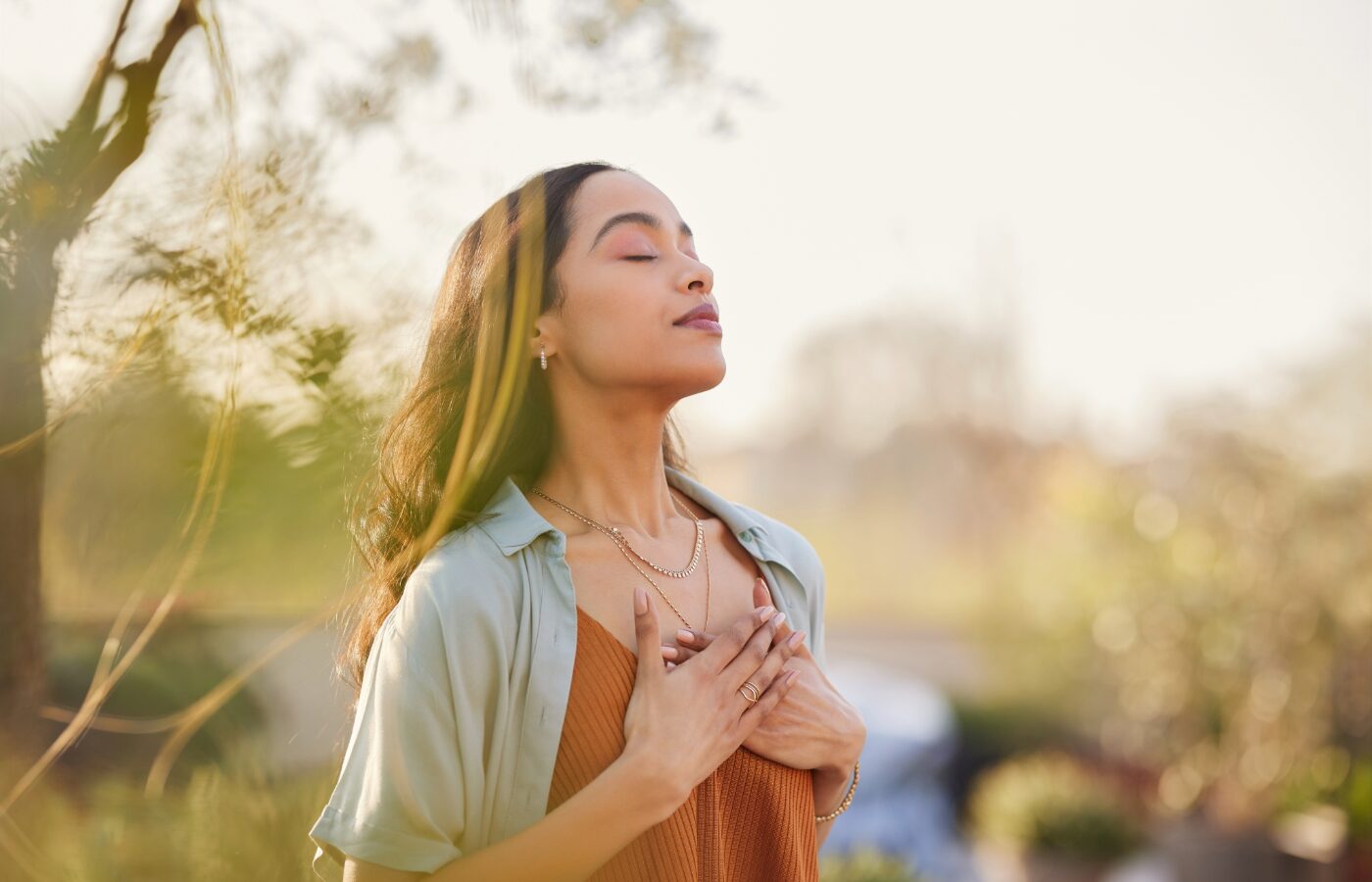 Photo of a black woman with her hand on her chest and breathing deeply against an outdoor abstracted background