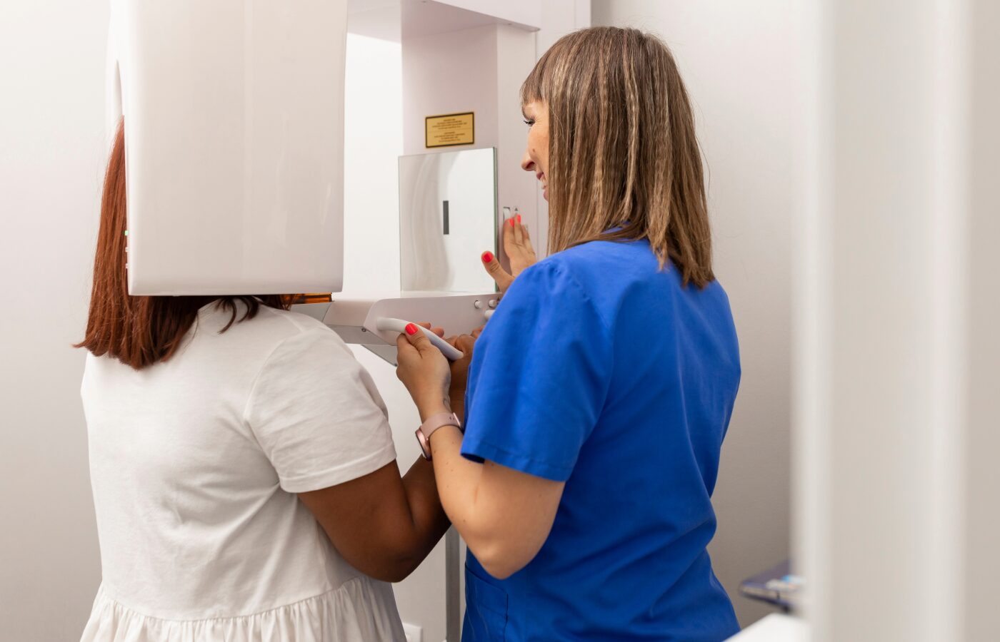 Woman standing in a CBCT scanner with dental tech helping her set up