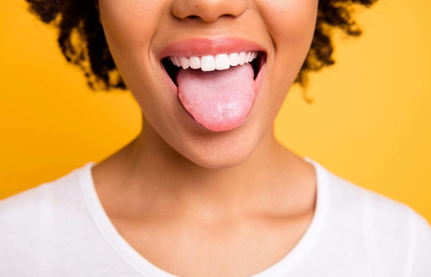 black woman with mouth open and tongue out on a yellow background with a white shirt