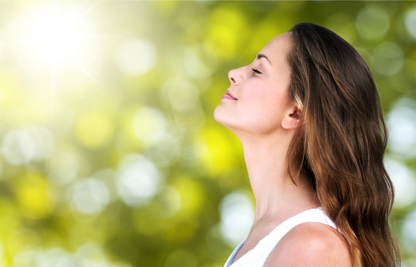 woman breathing through nose outside with trees all around and sunlight filtering through