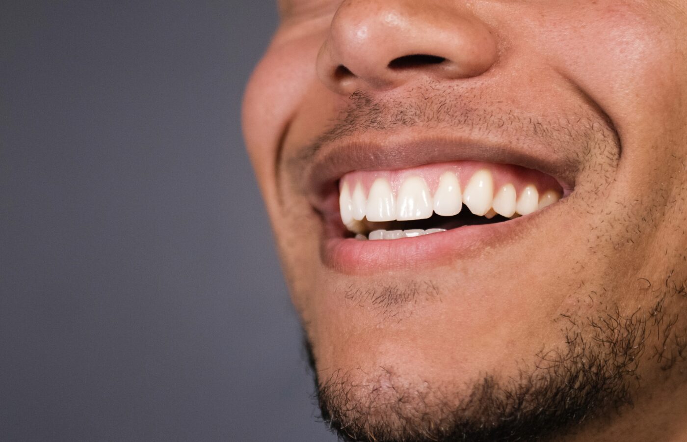 black mans lower face with healthy teeth and gums against gray background