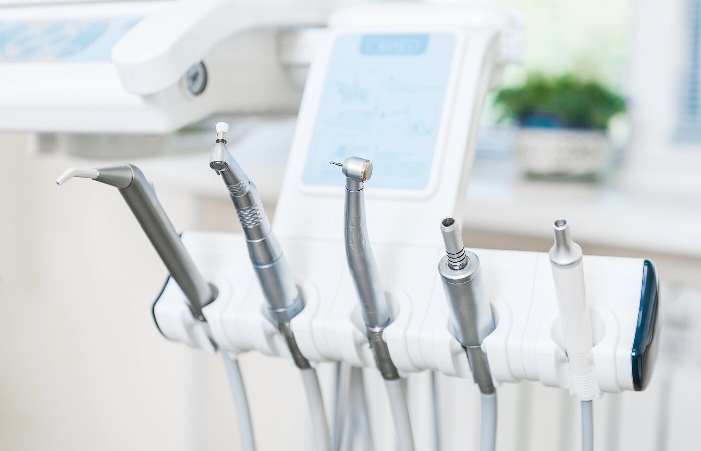 dental tools in their holder in the foreground with a window and plant blurred in the background